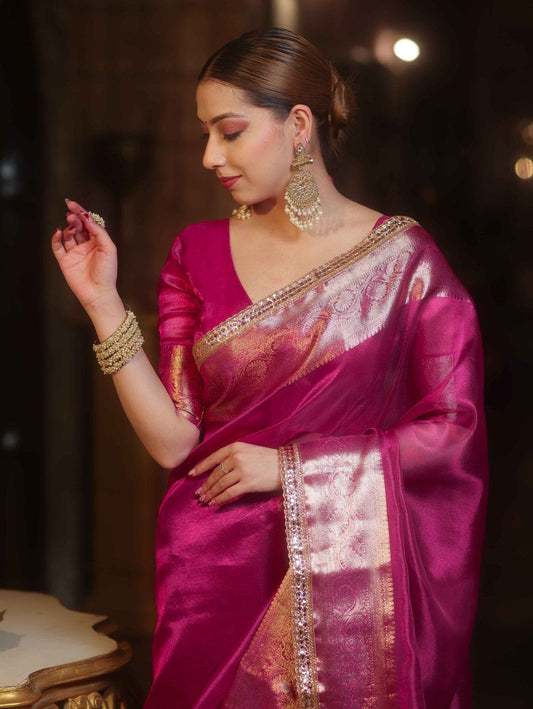 Woman in a pink saree with gold details against a dark background