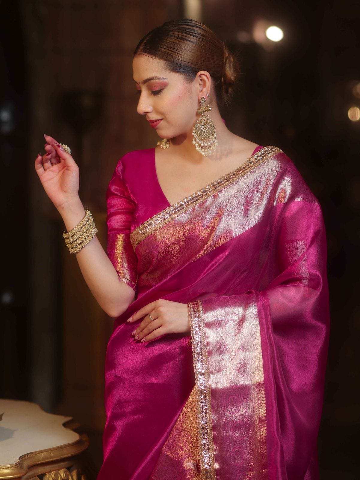 Woman in a pink saree with gold details against a dark background